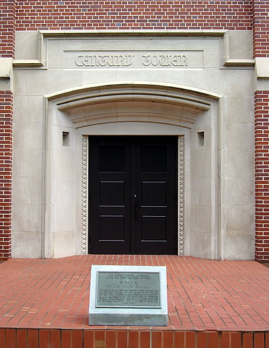 Red brick building facade with a light stone arched entrance and dark wood double doors. A plaque is below the entrance.